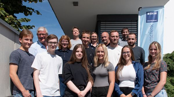Die Auszubildenden von IFB Eigenschenk und ihre Ausbilder stehen vor dem Firmengebäude auf einer Treppe für ein Gruppenbild und lachen in die Kamera