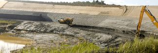 Zwei Bagger arbeiten an einem Hang nahe einem Gewässer und bewegen Erde auf einer Baustelle mit natürlicher Umgebung