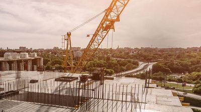 Luftaufnahme einer Baustellt mit einem Kran, im Hintergrund eine Stadt mit Autobahnen und Grünflächen