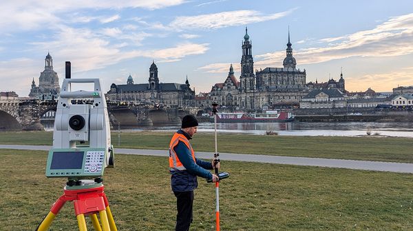 Ein Vermesser und ein Vermessungsgerät vor der Skyline von Dresden