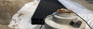 Baustelle mit Beton-Schachtbauwerk und orangefarbenem Gitter sowie schwarzen Kunststoffmodulen zur Regenwasserbewirtschaftung.