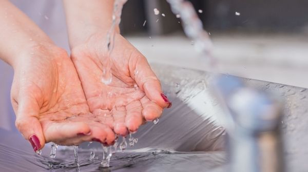Eine Person hält ihre Hände unter einen Wasserhahn, um daraus Trinkwasser aufzufangen.