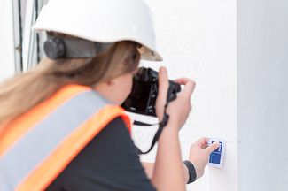 Die Duale Studentin Annalena bei der Arbeit draußen während sie in einen Riss an einer Mauer fotografiert.