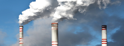 Drei Industrieschornsteine stoßen weiße Rauchwolken in den Himmel