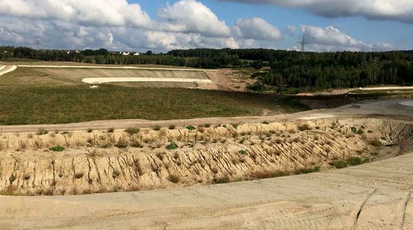 Im Vordergrund die Aschedeponie Westfeld Schwandorf, im Hintergrund Wald und blauer, bewölkter Himmel