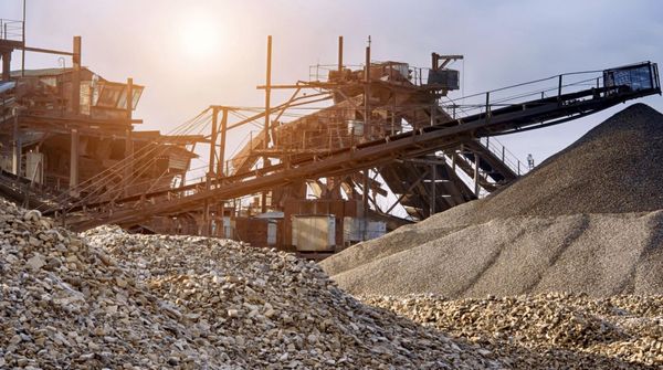 Ein Industriegelände mit Förderbändern und großen Schotterhaufen bei Sonnenlicht.