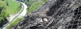 Ein steiler Hang ist mit Drahtnetzen und Verankerungen gesichert, um Steinschläge zu verhindern.