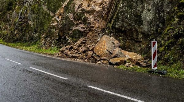 Felssturz entlang einer Straße mit herabgefallenen Steinen vom steilen, bewachsenen Felshang.