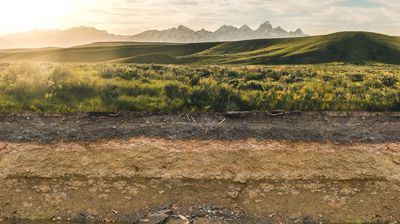 Verschiedene Bodenschichten, im Hintergrund sind Hügel, Berge und die Sonne zu erkennen