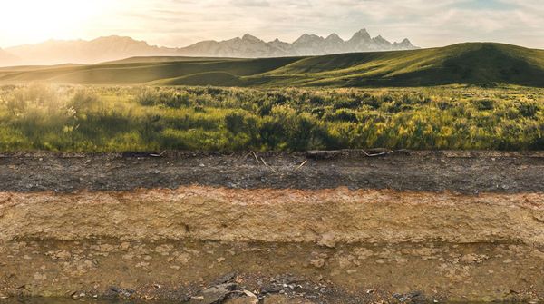 Verschiedene Bodenschichten, im Hintergrund sind Hügel, Berge und die Sonne zu erkennen