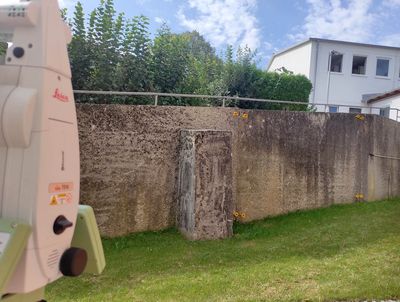 Detailaufnahme eines Vermessungsgeräts, das auf markierte Punkte an einer Betonwand im Freien ausgerichtet ist.