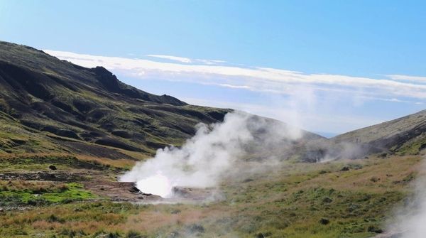 Dampf steigt aus dem Boden einer geothermisch aktiven Landschaft, was auf natürliche Erdwärmequellen hindeutet.