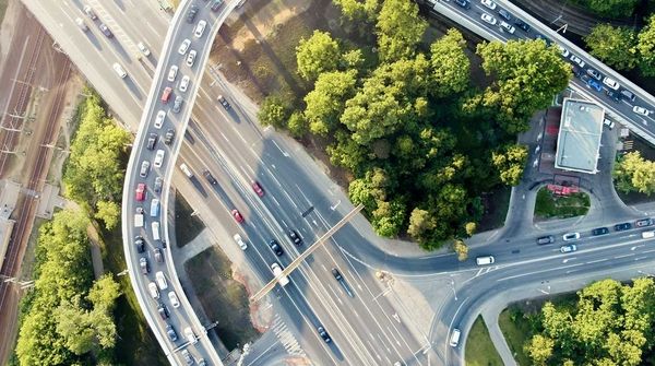 Luftaufnahme einer großen Straßenkreuzung mit dichtem Verkehr, mehreren Spuren und umliegenden Grünflächen.