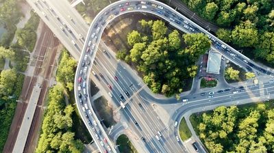 Luftaufnahme einer großen Straßenkreuzung mit dichtem Verkehr, mehreren Spuren und umliegenden Grünflächen.