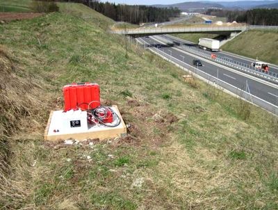 Rote Messgeräte und Kabel auf einer weißen Plattform am begrünten Autobahnböschungsrand.