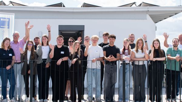 Die Azubis und ihre Ausbilder stehen auf der Dachterrasse und winken