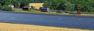 Ein großes Solarfeld erstreckt sich neben einer vielbefahrenen Landstraße.