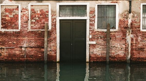 Alte, beschädigte Backsteinwand mit Tür und Fenstern, unterer Bereich vom Wasser überflutet