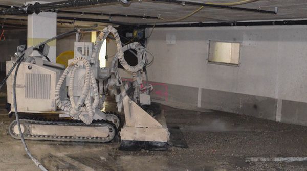 In einer Tiefgarage steht eine große Baumaschine, die den Boden aufarbeitet und Schutt verteilt.